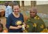 Auf dem Foto sind mehrere Personen in einem Dorf zu sehen. Zwei Frauen halten eine Packung Nelken in der Hand.
