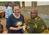Ein Foto in einem Dorf in Tansania, auf dem mehrere Personen zu sehen sind. Eine Frau hält eine Packung Nelken in der Hand.