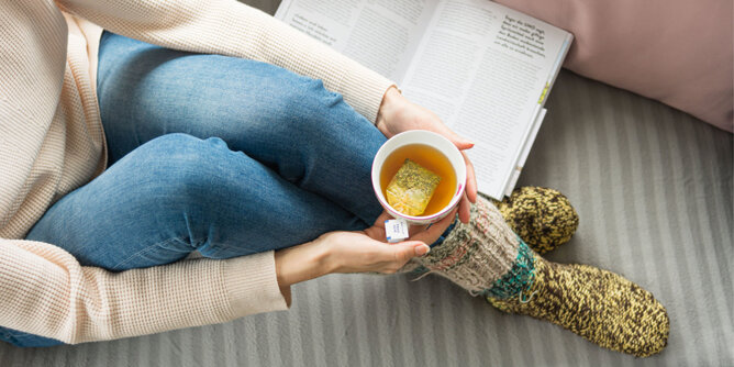 Foto von einer Frau auf der Couch mit einer Tasse Tee und einem Buch. | © SONNENTOR