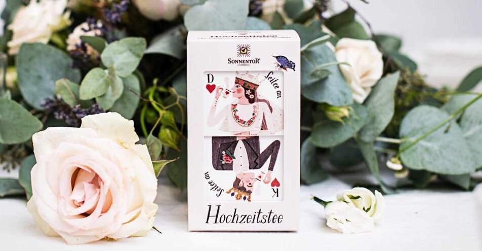 Photo of a package of wedding tea. The tea is on a table with flowers in the background. | © SONNENTOR