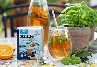 Foto einer Packung Kühle Kanne Orange-Basilikum Tee. Daneben sieht man den fertigen Eistee. | © SONNENTOR