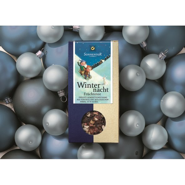 Foto einer Packung Winternacht Tee lose, die auf blauen Christbaumkugeln liegt.