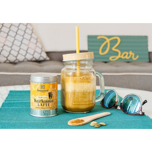 In the photo you can see an Iced Turmeric Latte in a glass. Next to it is the turmeric latte vanilla tin.