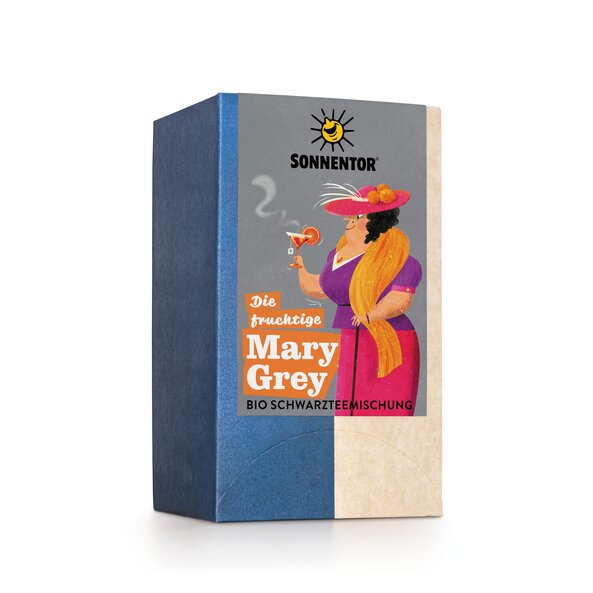 Mary Grey ist mit einem pinken Rock und einer violetten Bluse mit orangem Schal und pinken Hut gekleidet und trinkt ihren dampfenden Tee aus einem Cocktailglas.