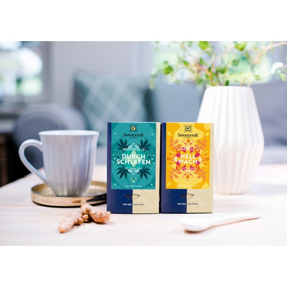 You can see the two Happiness Is teas Feeling Wide Awake and A Restful Sleep. They are placed side by side on a table, next to them a ginger tuber and a cup.