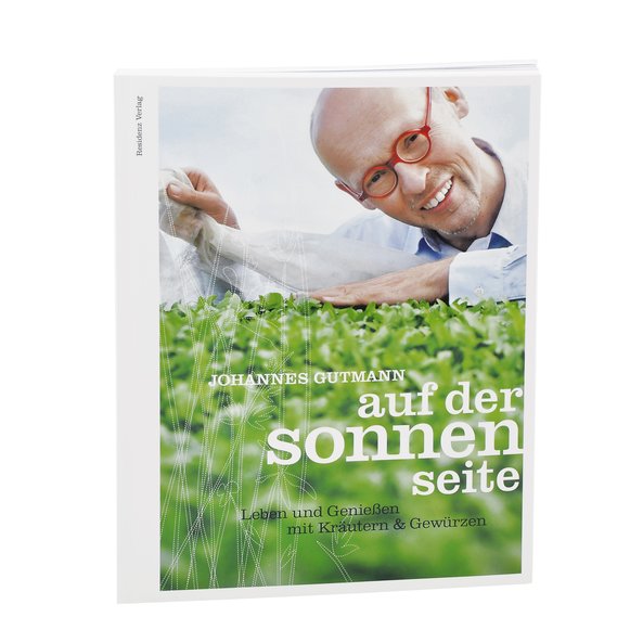 The photo shows the book Auf der Sonnenseite. It shows Johannes Gutmann with his red glasses in front of a salad garden.