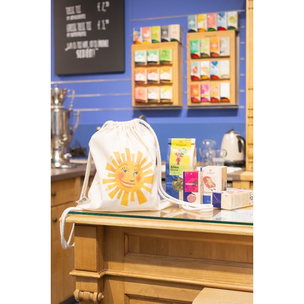 Shown is a cotton gym bag printed with a sun. The gym bag is in a Sonnentor store with teas in the background.