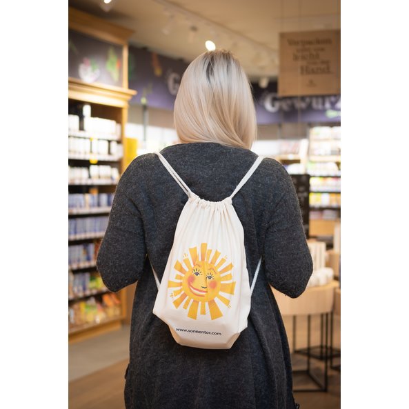 Abgebildet ist ein Baumwoll Turnbeutel mit einer Sonne bedruckt. Eine Frau trägt ihn am Rücken.