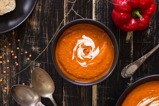 Auf dem Foto ist ein Schälchen mit Paprikaschaumsuppe zu sehen. Daneben liegen Paprika, Linsen und zwei Löffel. | © SONNENTOR
