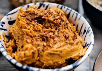  The spiced butter is a rich orange color and is in a bowl decorated with loose spices. | © SONNENTOR