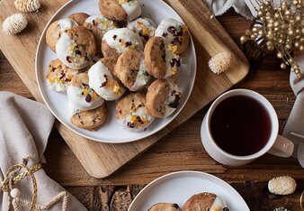 Ein Teller mit Panettone Keksen steht auf einem Brett inmitten von einem weihnachtlich dekoriertem Umfeld mit einer Tasse Kaffee und einem Teelicht.  | © SONNENTOR