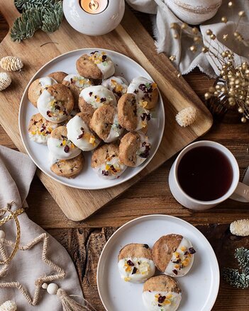 Ein Teller mit Panettone Keksen steht auf einem Brett inmitten von einem weihnachtlich dekoriertem Umfeld mit einer Tasse Kaffee und einem Teelicht.  | © SONNENTOR