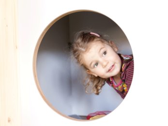 In the photo you can see a child looking out of a round hole. | © SONNENTOR